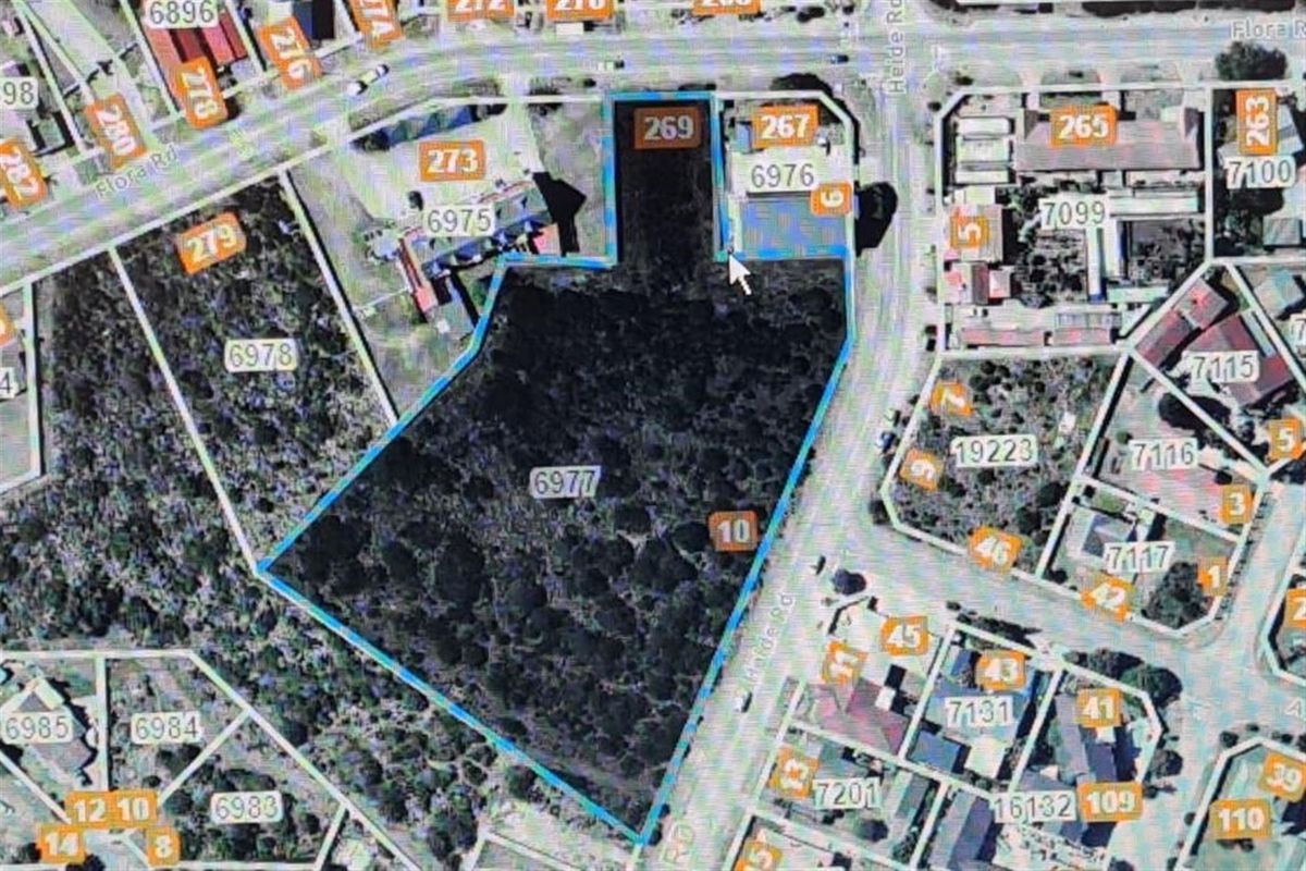An aerial view of a vacant commercial land plot, highlighted with blue boundaries, showing its location and surrounding street infrastructure.