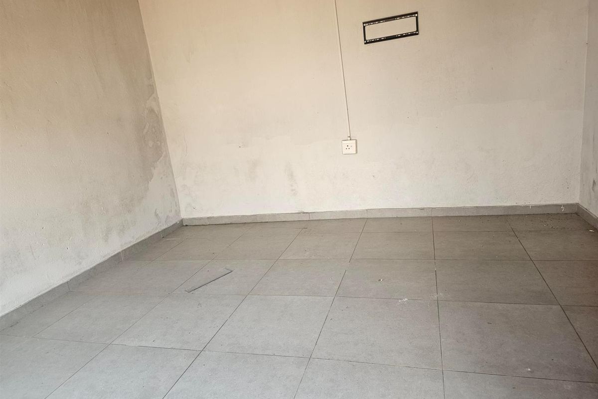 An empty room featuring neutral floor tiles and a wall-mounted television bracket, requiring cosmetic updates to the wall surfaces.