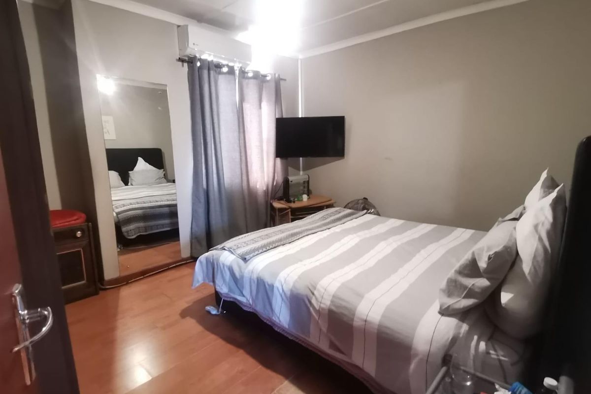 A functional bedroom featuring laminate flooring, a wall-mounted air conditioning unit, and a large floor-to-ceiling mirror.