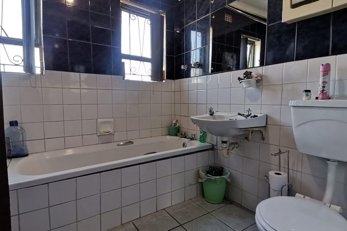 A functional bathroom featuring a bathtub, wall-mounted basin, and toilet, finished with a combination of dark and white wall tiling.