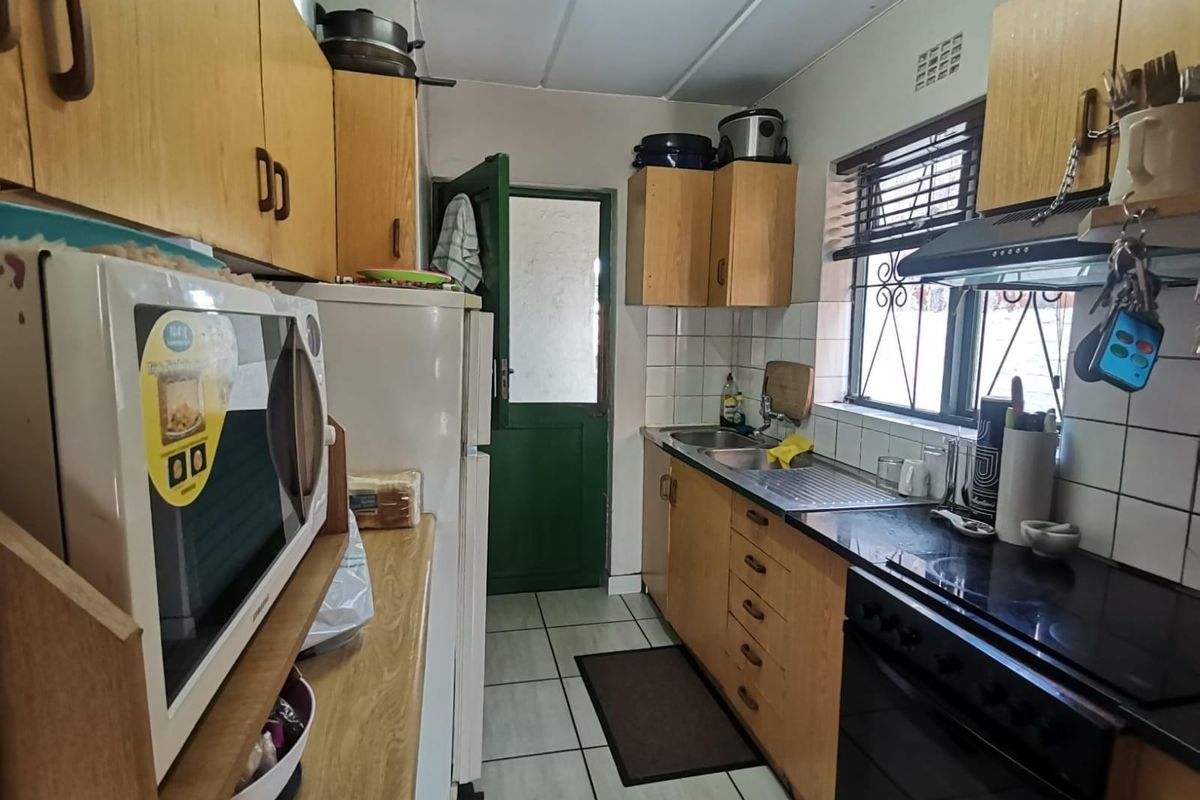 A functional galley-style kitchen featuring wood-veneer cabinetry, integrated oven and hob, tiled flooring, and direct access to the exterior.