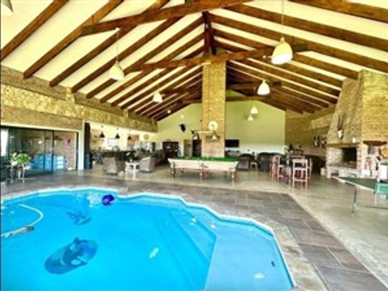 Spacious indoor entertainment area featuring a large swimming pool, exposed timber roof trusses, and a prominent stone fireplace.