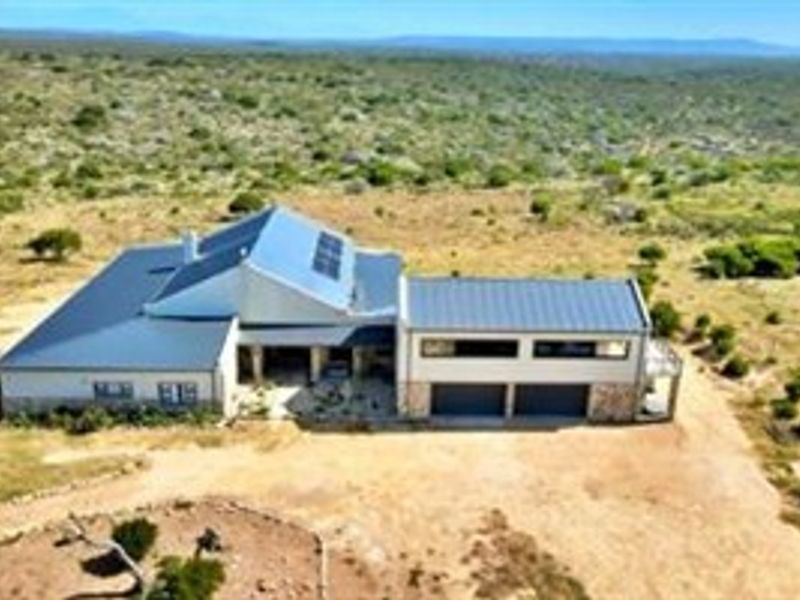 Aerial view of a modern farm residence featuring a metal roof with solar panels, stone cladding, and an attached double garage set in landscape.