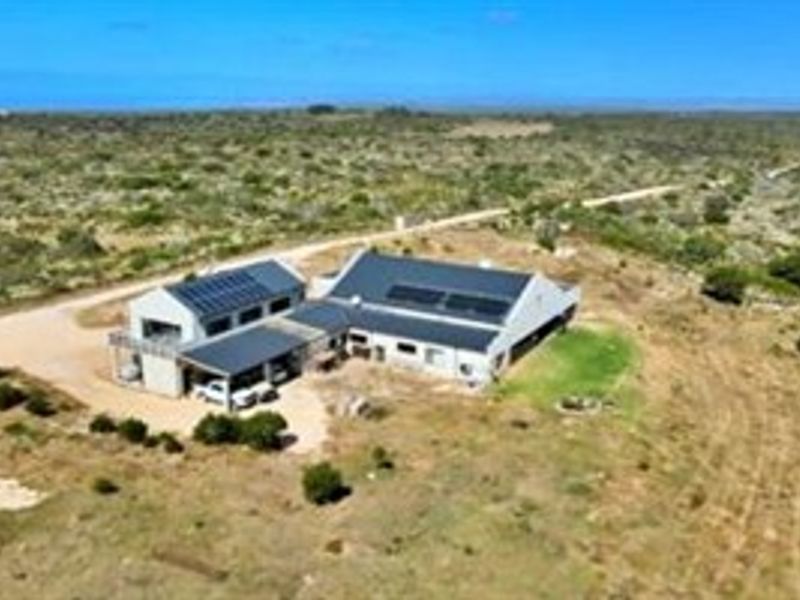Aerial view of a rural farm property featuring a main dwelling with solar panels, a metal roof, and an attached carport.