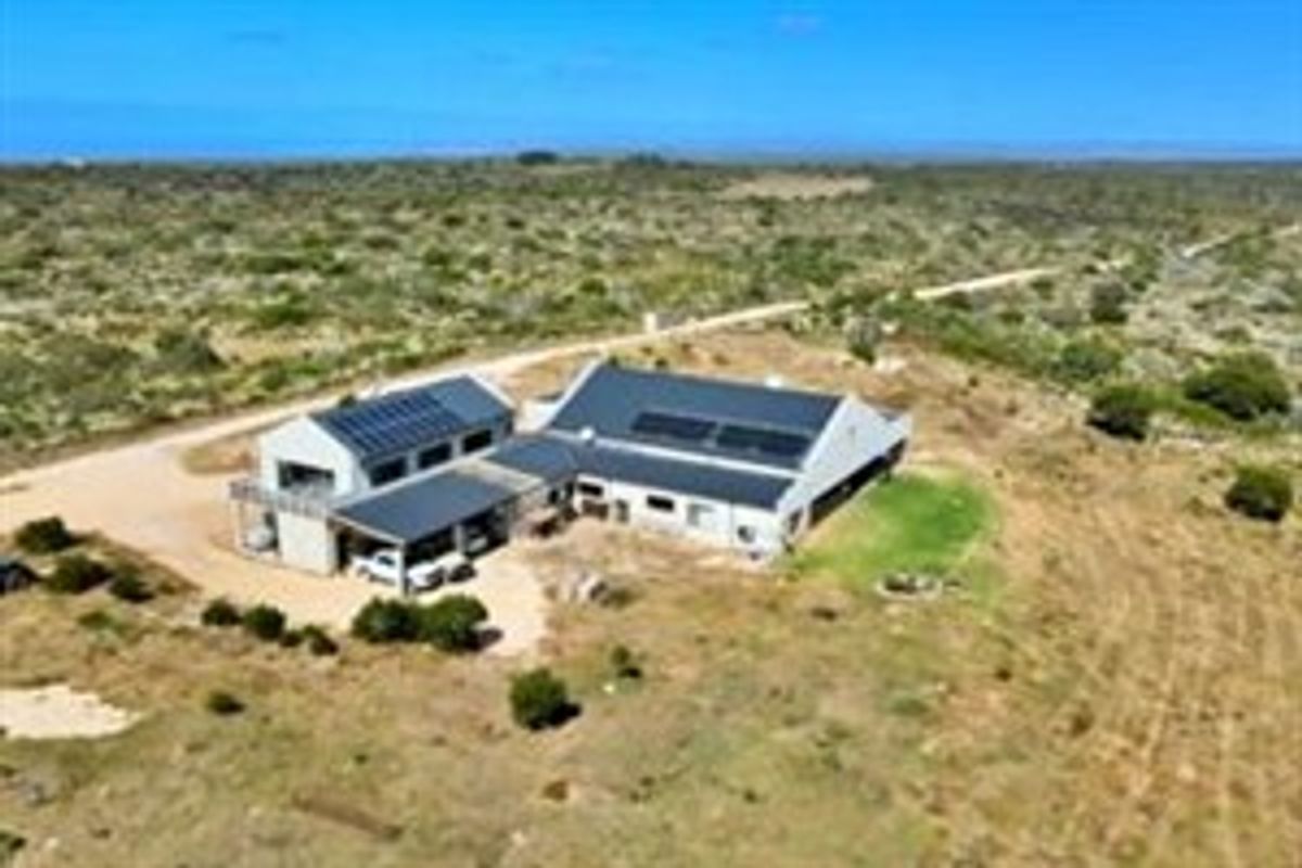 Aerial view of a rural farm property featuring a main dwelling with solar panels, a metal roof, and an attached carport.