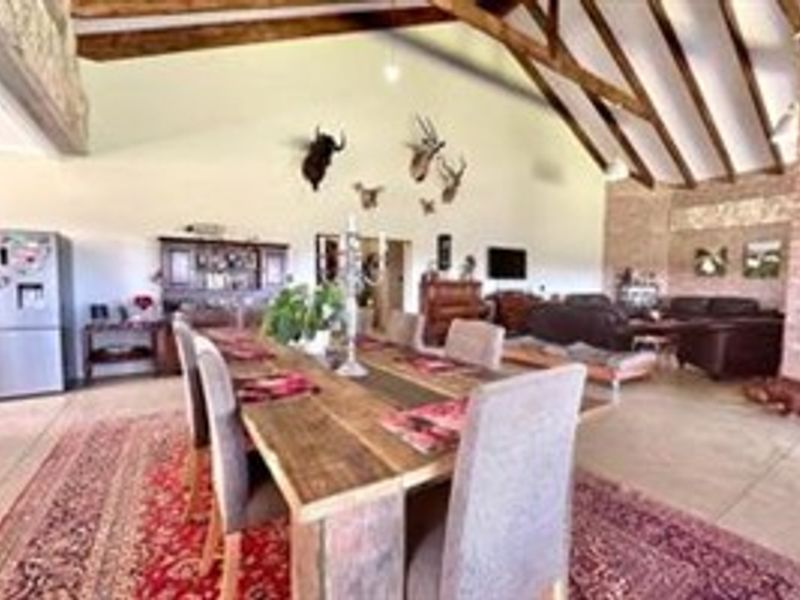 Spacious open-plan living and dining area featuring a high vaulted ceiling with exposed timber trusses and a rustic exposed brick feature wall.
