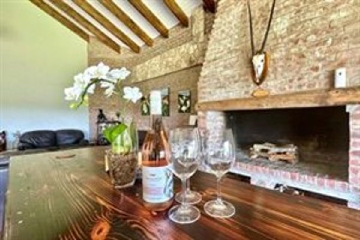Rustic living area featuring a prominent brick fireplace with a timber mantelpiece and exposed wooden ceiling beams.