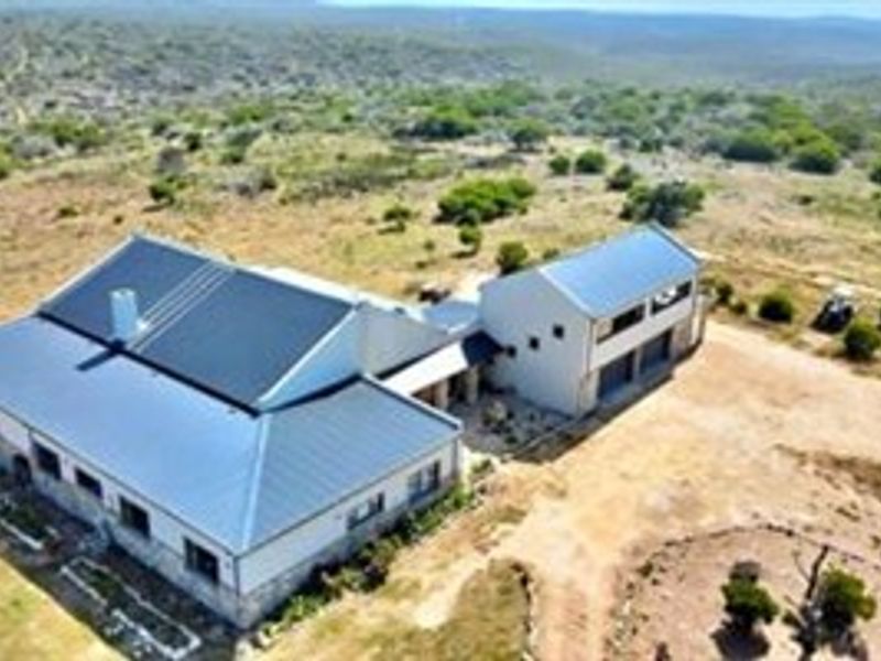 Aerial view of a farm property featuring a main dwelling with a metal roof and attached garage structure set in a rural landscape.