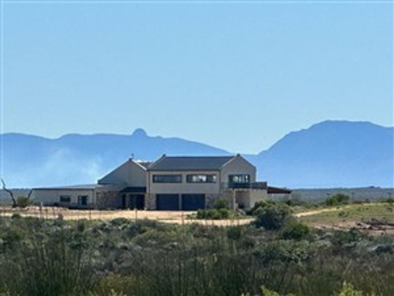 A distant view of a modern farmhouse featuring stone cladding, a pitched roof, and an integrated double garage set against a scenic mountain backdrop.