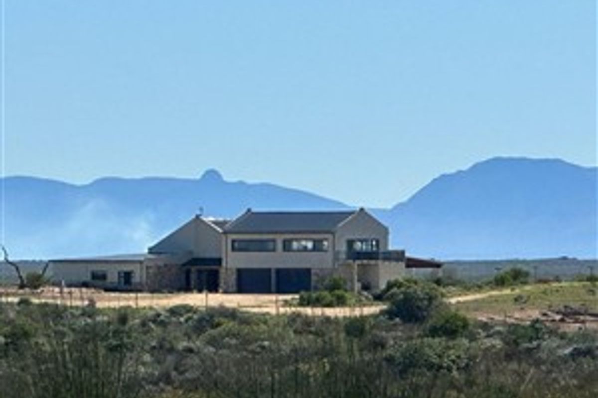 A distant view of a modern farmhouse featuring stone cladding, a pitched roof, and an integrated double garage set against a scenic mountain backdrop.