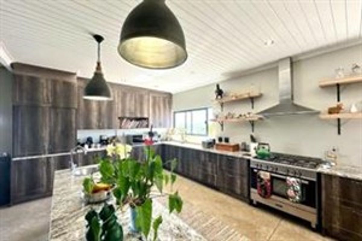 Modern kitchen featuring dark wood cabinetry, stone countertops, a large central island, open shelving, and a professional-style gas range with stainless steel extractor.