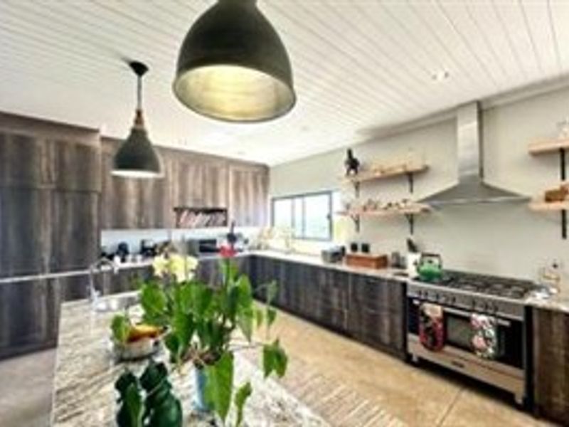 Modern kitchen featuring dark wood cabinetry, stone countertops, a large central island, open shelving, and a professional-style gas range with stainless steel extractor.
