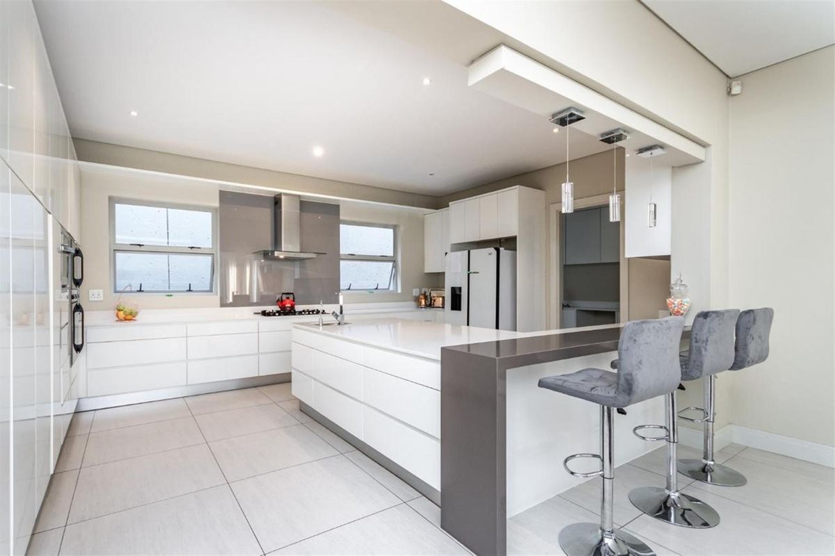 Modern kitchen featuring a large central island with breakfast bar, sleek white cabinetry, stone countertops, integrated appliances, and recessed ceiling lighting.