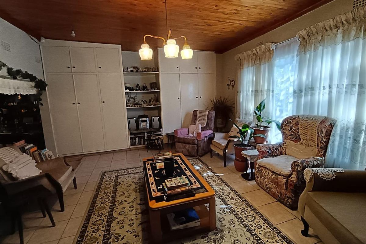 A living room featuring a wood-paneled ceiling, built-in floor-to-ceiling cabinetry with integrated shelving, and tiled flooring.