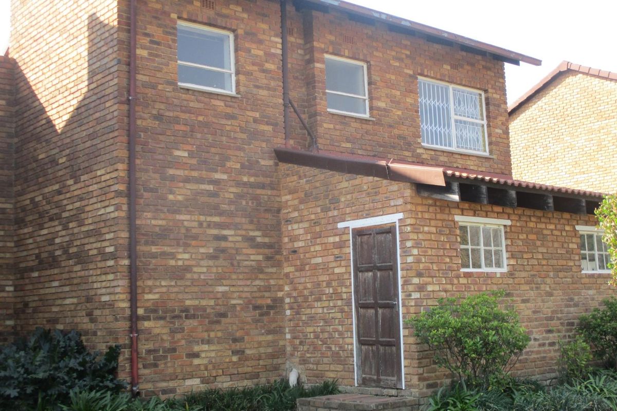 A view of the rear exterior facade featuring face brick construction, a timber door, and security bars on the windows.