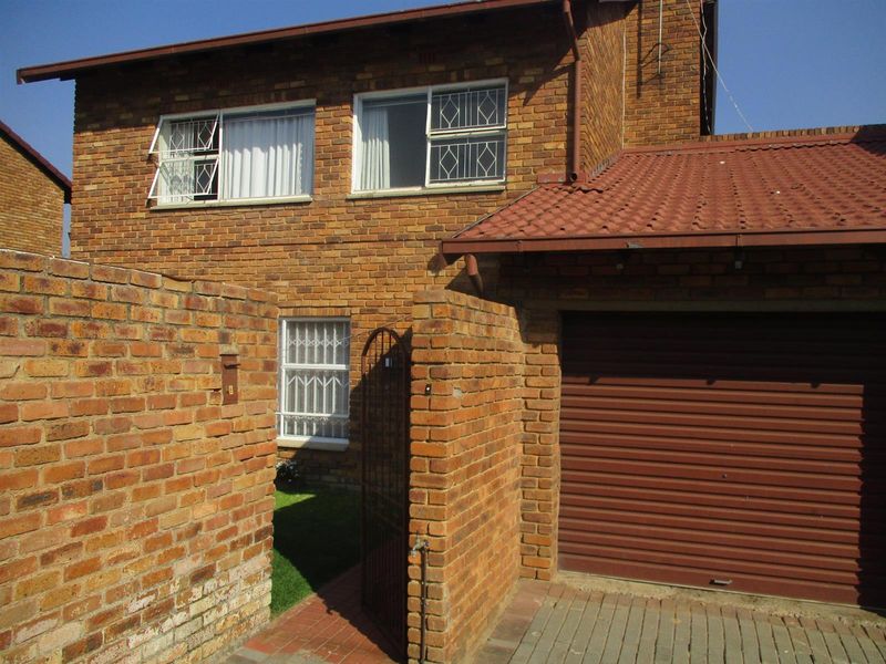 Front elevation of a double-story face brick house featuring a roller shutter garage door, security bars on windows, and a brick boundary wall.