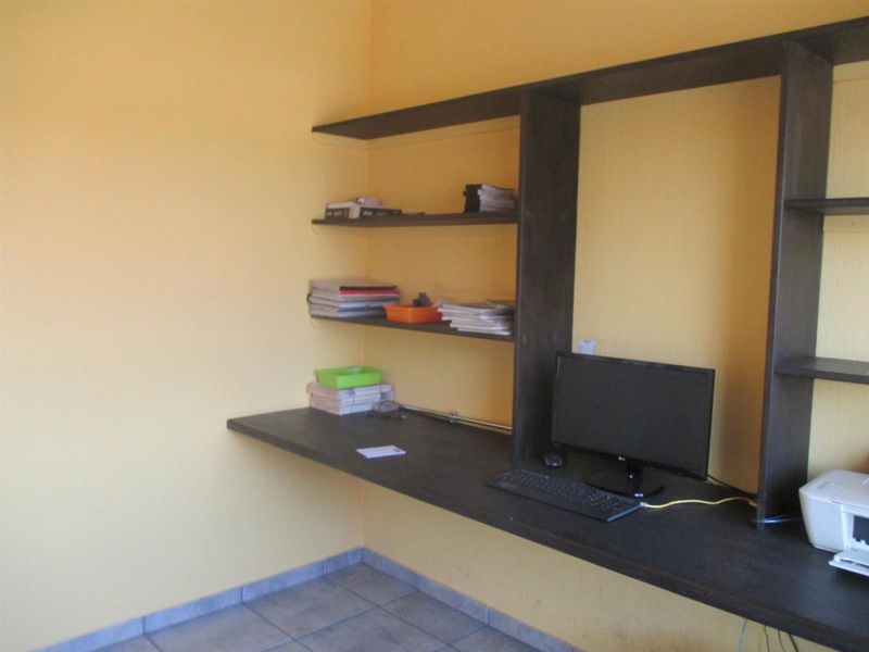 A functional home office space featuring built-in dark wood shelving and a matching desk, set against yellow walls with tiled flooring.