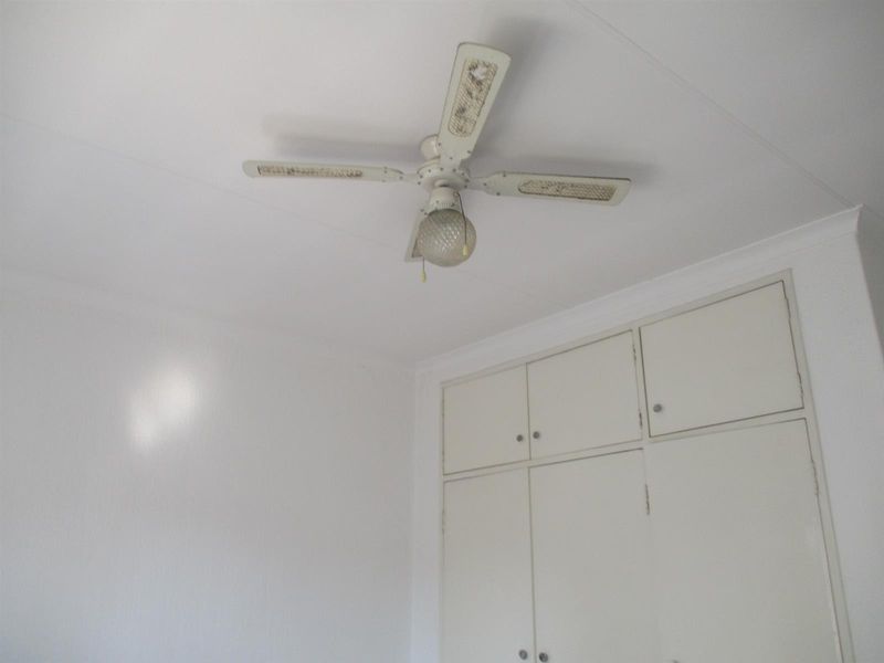 A simple bedroom interior featuring built-in cupboards and a ceiling fan, presenting a clean, neutral space ready for personalization.