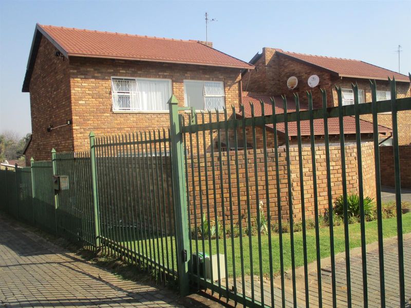 Front view of a face brick residential property featuring a tiled roof, secure steel perimeter fencing, and paved driveway access.