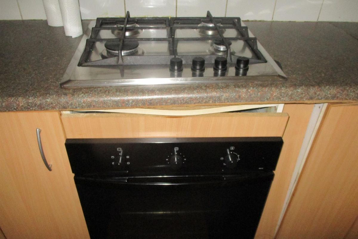 Close-up view of a kitchen cooking station featuring a gas hob, built-in oven, and laminate countertops with visible damage to the cabinetry trim.