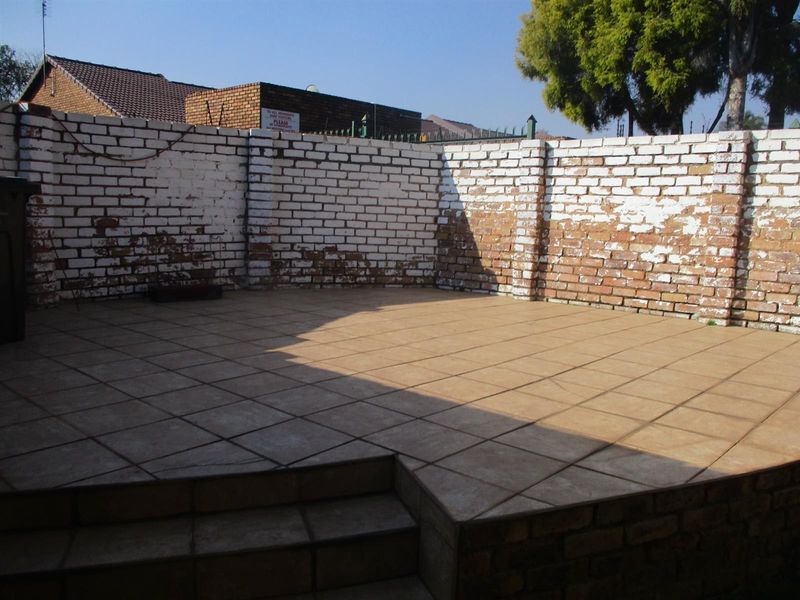 An open-air tiled patio area featuring a raised platform and a perimeter brick wall with visible weathering and paint deterioration.
