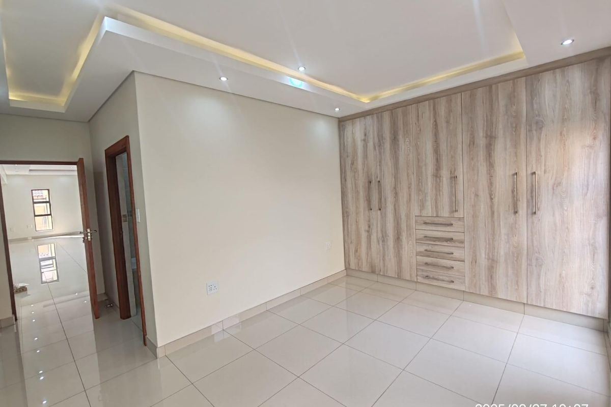 A bright, modern bedroom featuring large built-in wooden wardrobes, recessed ceiling lighting, and polished floor tiles.