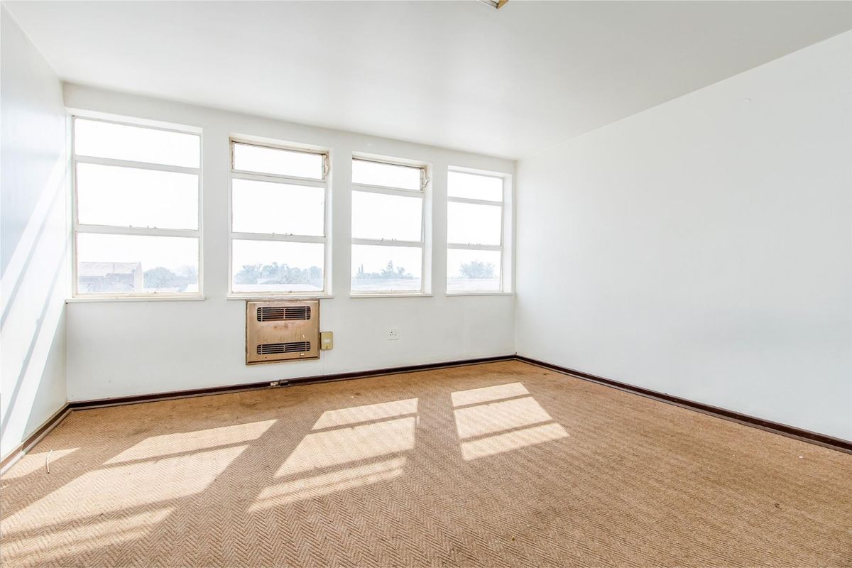 An empty room featuring large windows, a built-in air conditioning unit, and carpeted flooring, offering a bright and versatile space.