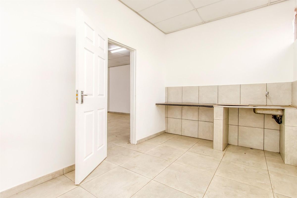 A functional kitchenette area featuring tiled splashbacks, a built-in counter, and a stainless steel sink, leading into an adjacent office space.