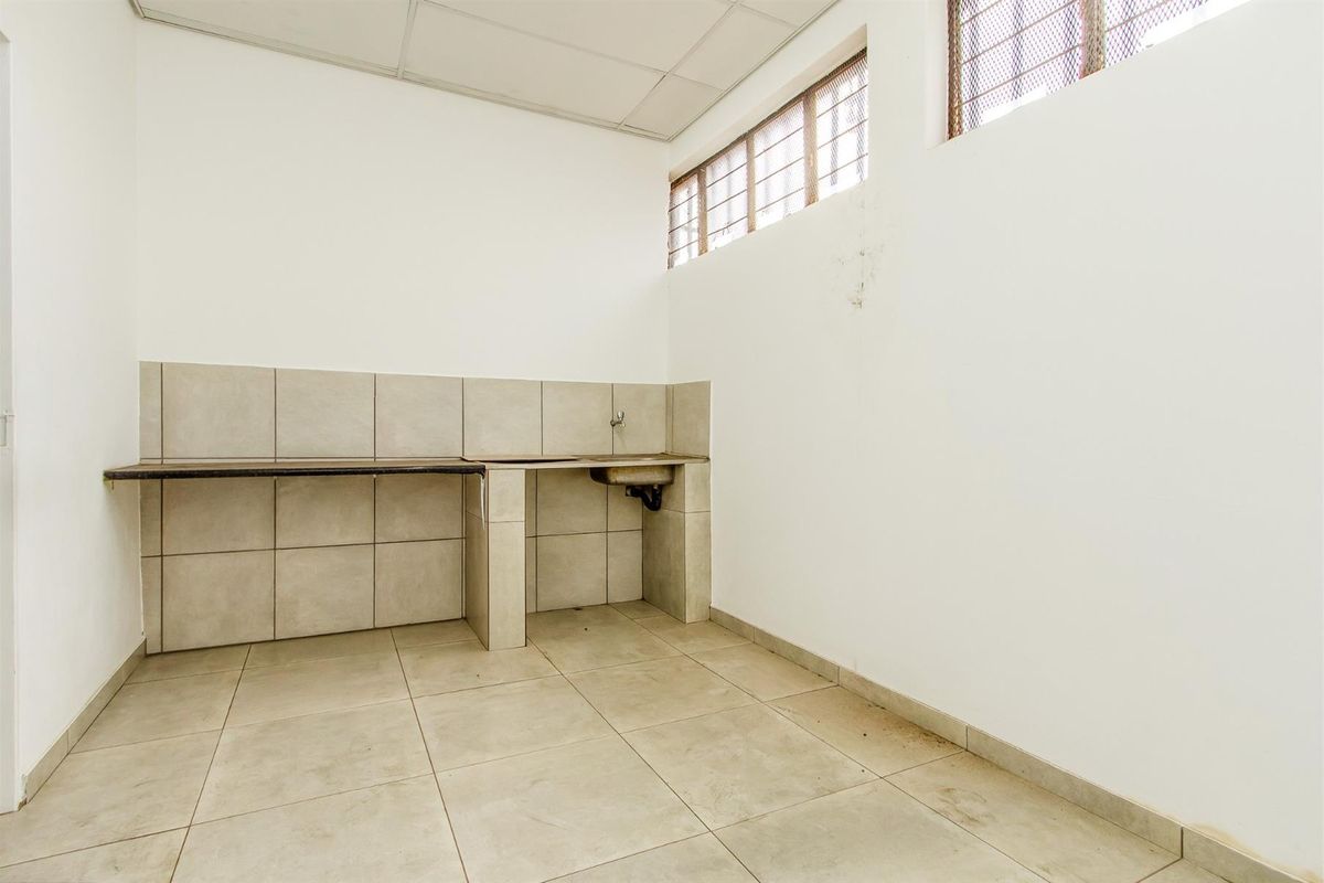 A functional, empty kitchen area featuring tiled flooring, a built-in counter with a sink, and high-level windows with security bars.