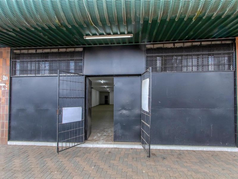 Commercial storefront entrance featuring heavy-duty metal security gates, a corrugated metal awning, and tiled facade detailing.