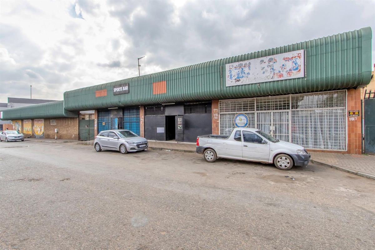 Front exterior view of a commercial property featuring a corrugated metal roof canopy, security gates, and large storefront windows.