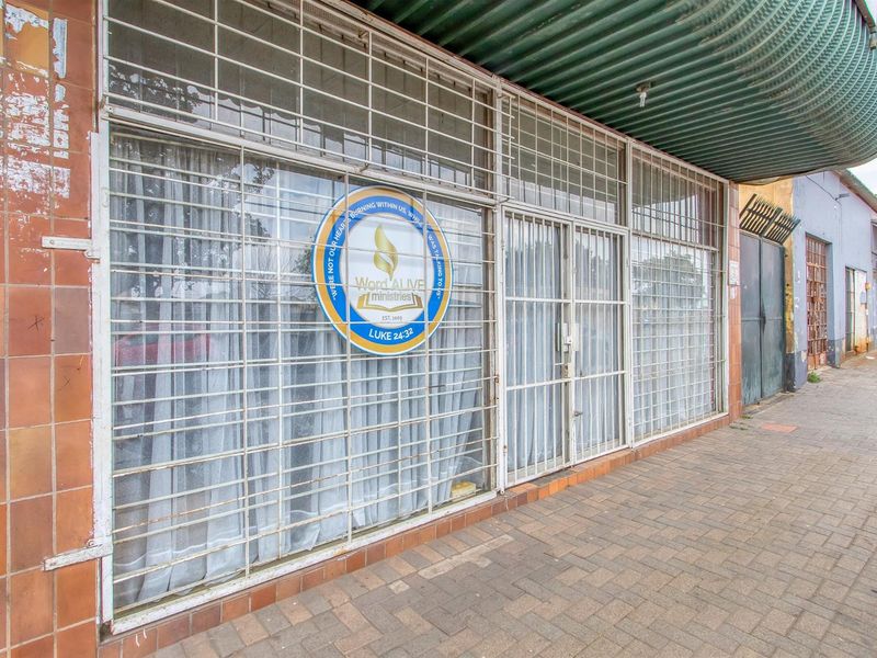 Commercial storefront featuring a tiled facade, security bars, and a corrugated metal awning, located along a paved sidewalk.