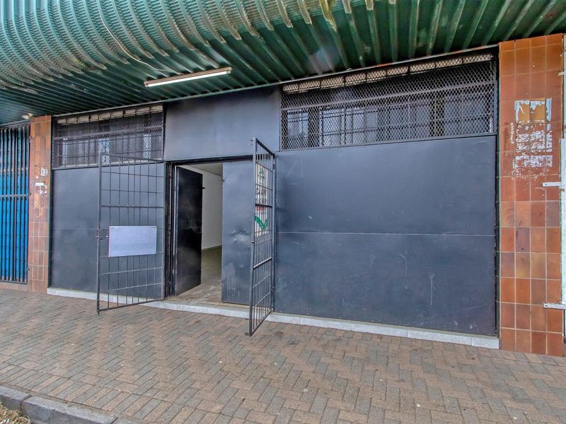 Commercial storefront entrance featuring heavy-duty security gates, metal shutters, and a corrugated awning, situated on a paved sidewalk.