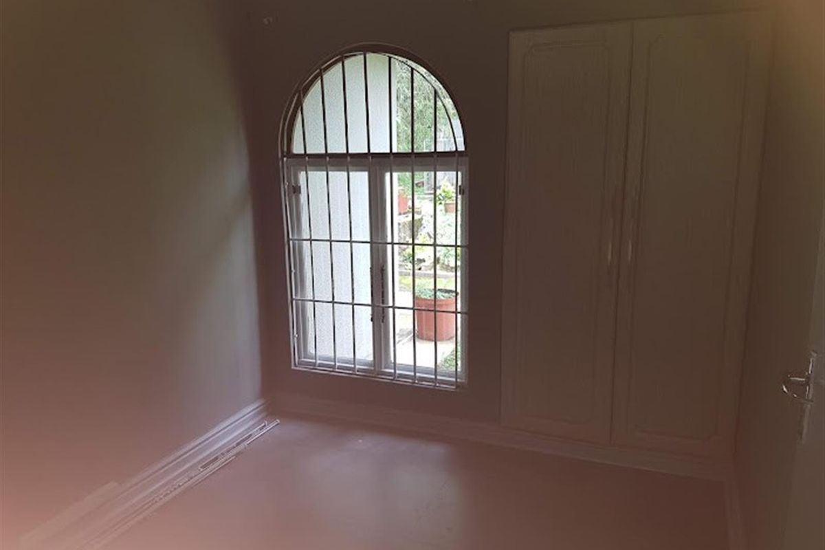 A vacant bedroom featuring a built-in wardrobe and an arched window with security bars, offering a neutral canvas for personalization.