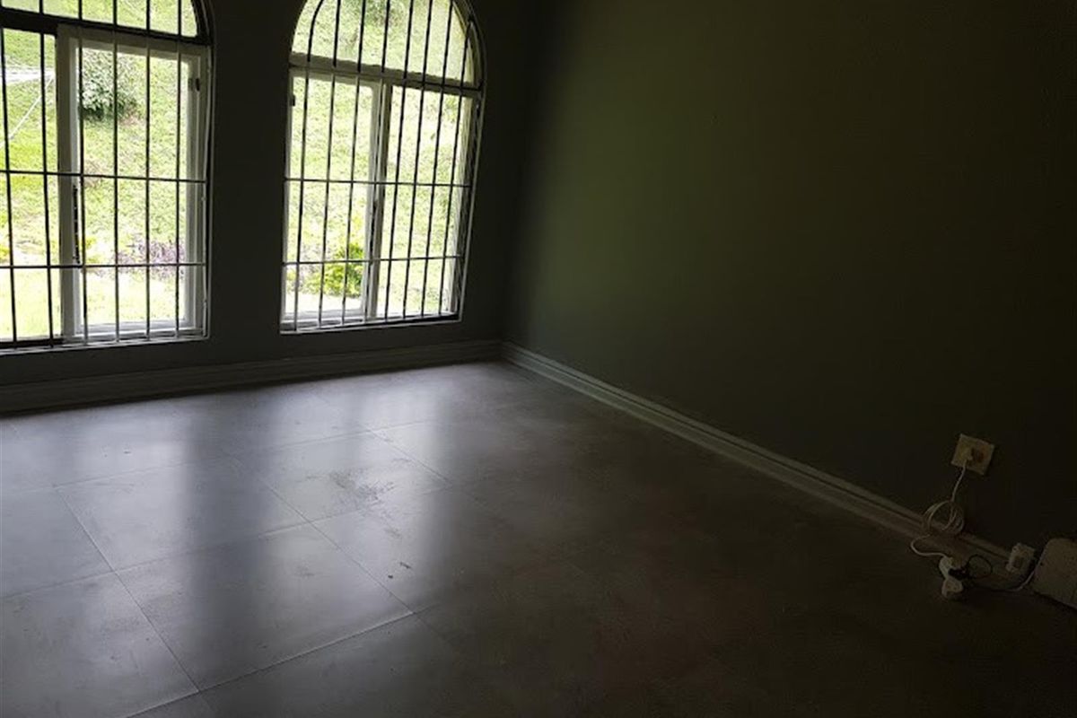 An empty room featuring large arched windows with security bars and neutral floor tiling, offering a blank canvas for interior design.