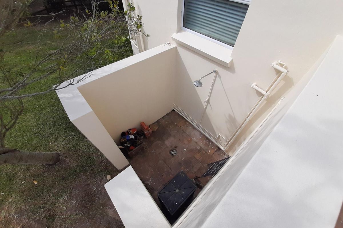 An outdoor shower area located at the rear of the property, featuring brick paving, drainage, and exposed plumbing fixtures.