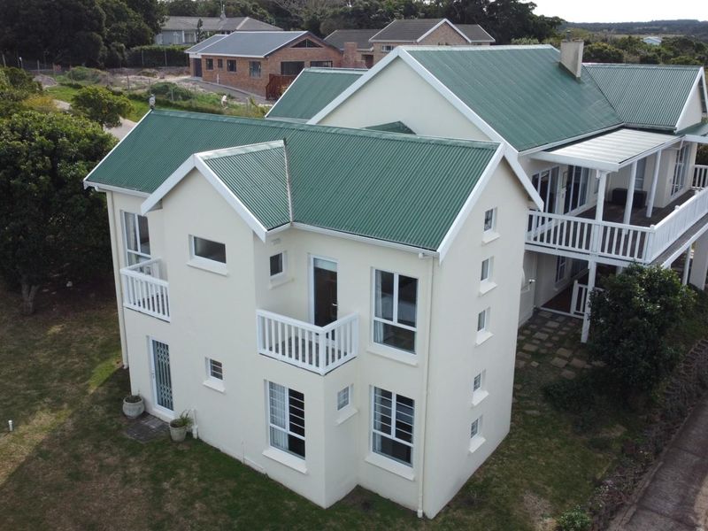 Aerial view of a two-story residential property featuring a green corrugated metal roof, multiple balconies, and surrounding garden space.