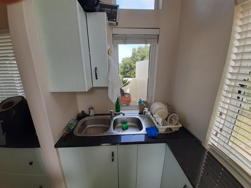 A compact scullery area featuring a double bowl stainless steel sink, granite countertops, and built-in cabinetry with natural light from a window.