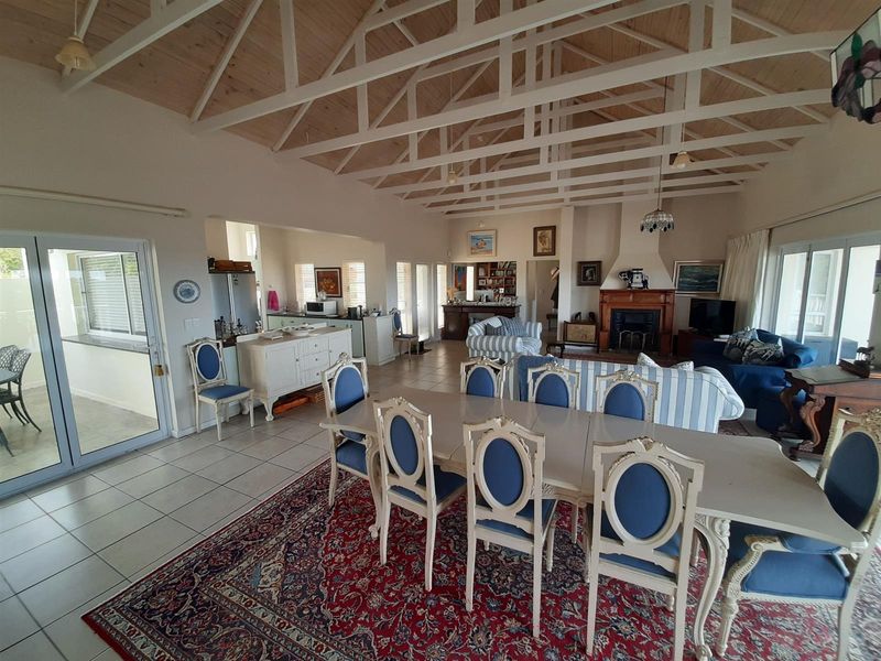 Spacious open-plan living and dining area featuring a high vaulted timber ceiling with exposed trusses, tiled floors, and a traditional fireplace.