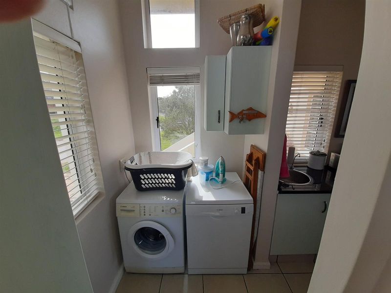 Compact laundry area featuring built-in cabinetry, a sink, and space for under-counter appliances, finished with tiled flooring and natural light.