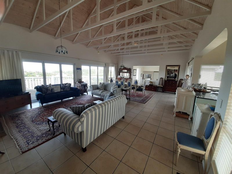Spacious open-plan living and dining area featuring high vaulted timber ceilings with exposed trusses, tiled floors, and large sliding doors leading to a balcony.