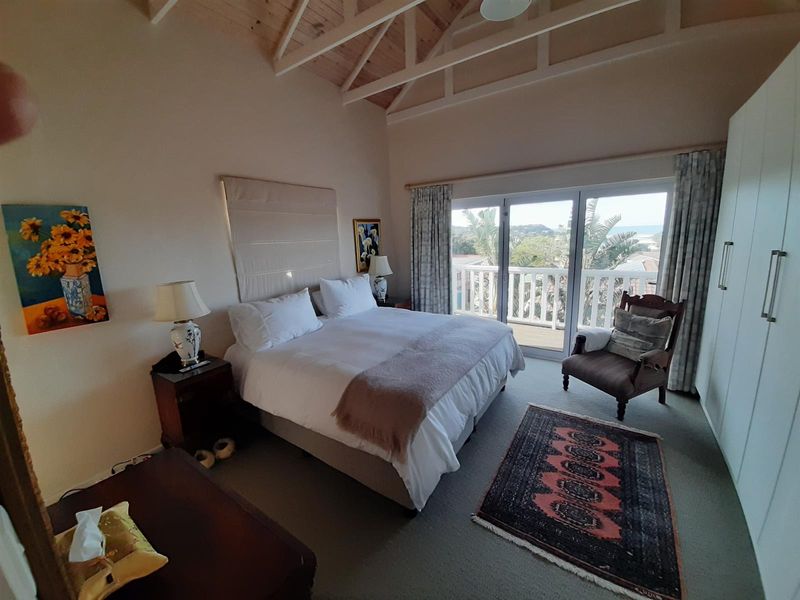 Spacious bedroom featuring a vaulted timber ceiling, built-in wardrobes, and sliding glass doors opening onto a private balcony with scenic views.