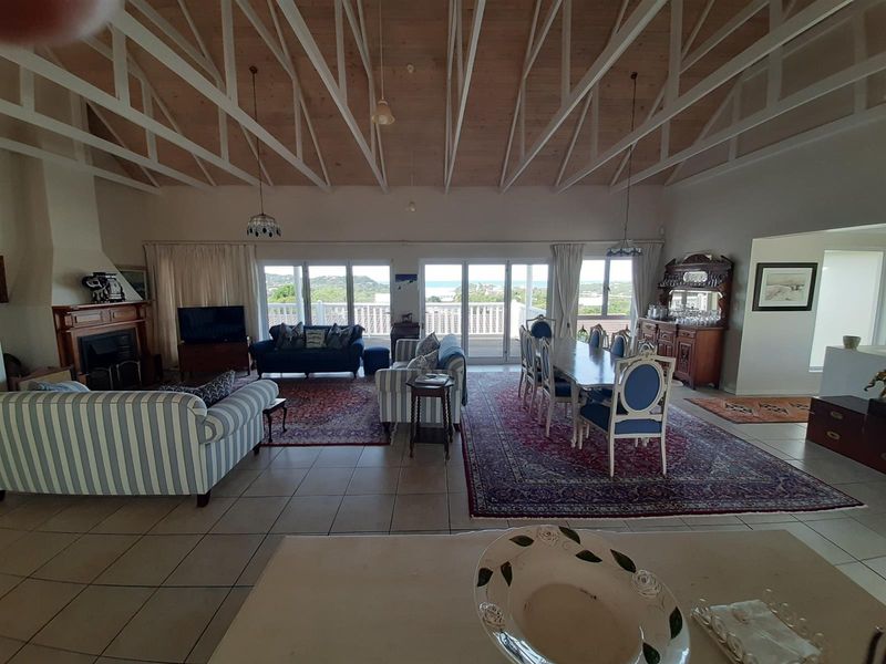 Spacious open-plan living and dining area featuring a high vaulted timber ceiling, exposed trusses, tiled floors, and large sliding doors leading to a balcony.