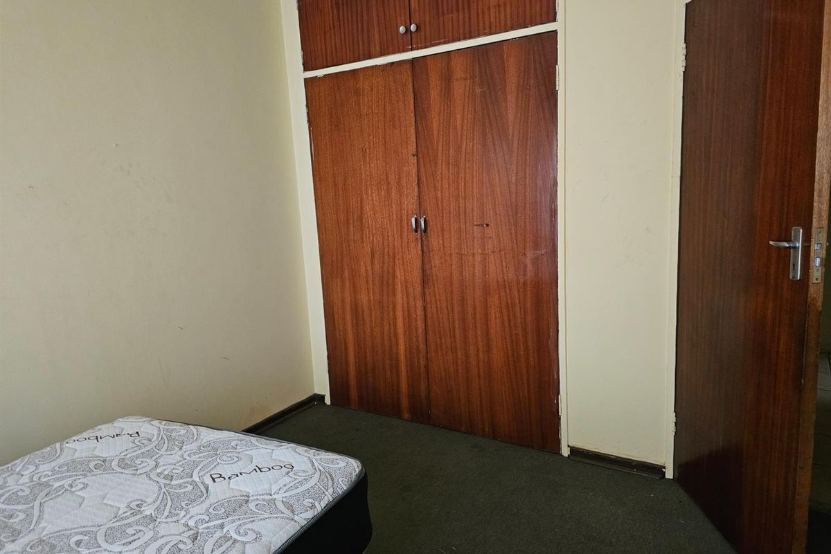 A bedroom featuring built-in wooden cupboards and carpeted flooring, offering a functional space in need of cosmetic updates.
