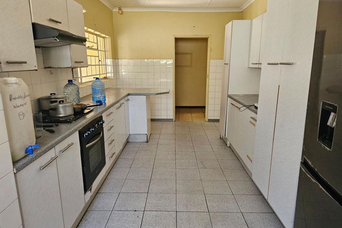 A functional kitchen featuring white cabinetry, tiled splashbacks, a built-in oven and hob, and tiled flooring, offering a practical layout for renovation.