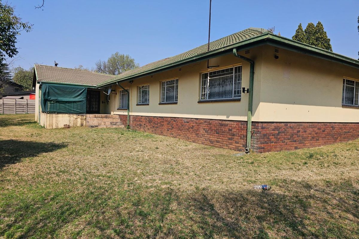 Rear view of a single-story house featuring a brick base, plastered walls, tiled roof, and a small raised patio area.