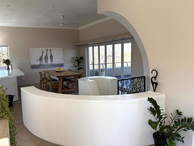 Open-plan living and dining area featuring a distinctive curved architectural wall, recessed ceiling lighting, and large glass sliding doors leading to an outdoor balcony.