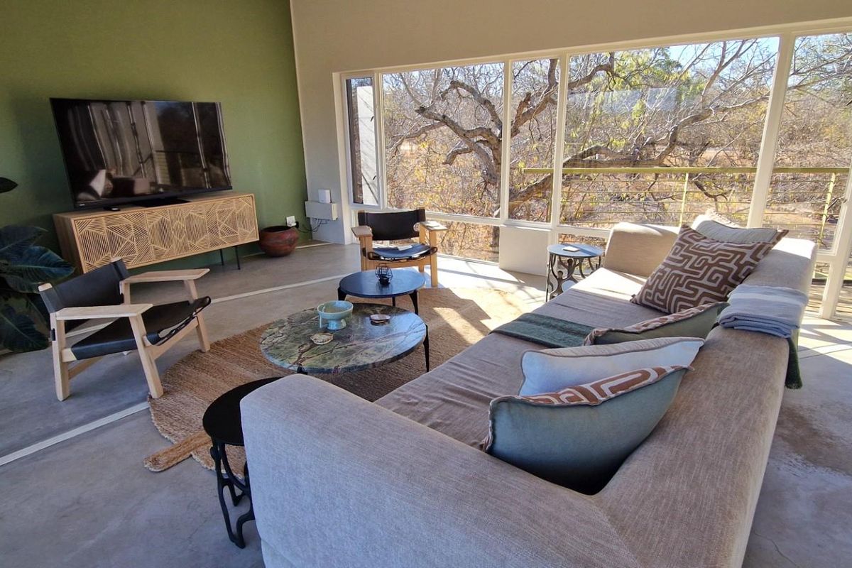 A bright living room featuring polished concrete floors, a large accent wall, and expansive floor-to-ceiling windows offering natural light and scenic outdoor views.