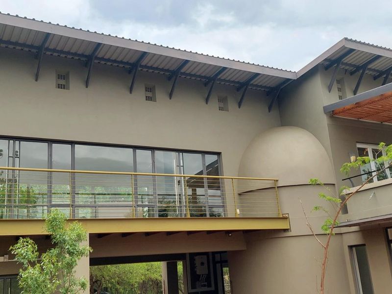 Rear elevation of a modern home featuring a spacious balcony with metal railings, large sliding glass doors, and a decorative timber pergola.