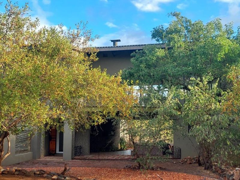 A two-story residential property featuring a covered ground-level patio and an upper-level balcony, surrounded by established trees and natural landscaping.